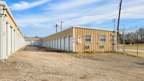 Tan storage facility with a gated fence and gravel road.