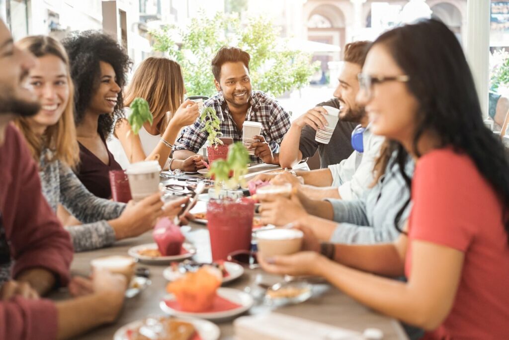 A group of friends enjoying drinks and food together at a food hall, smiling and sharing conversation.